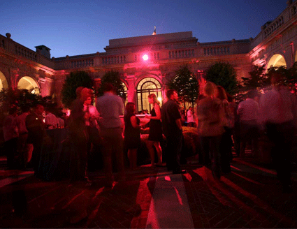 People dancing and mingling under a red light and dark blue sky in the Freer Courtyard at night.